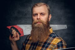 A bearded carpenter man dressed in a plaid shirt holds handsaw. Royalty Free Stock Photography A bearded carpenter man dressed in a plaid shirt holds handsaw. Royalty Free Stock Photography