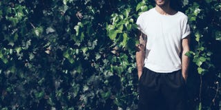 Bearded man with tattoo wearing blank white tshirt and black sunglasses.Green garden wall background. Wide closeup