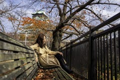 Beautiful asian woman enjoyed sitting on a wooden branch in the autumn garden with Osaka castle in background royalty free stock image Beautiful asian woman enjoyed sitting on a wooden branch in the autumn garden with Osaka castle in background royalty free stock image