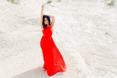 Beautiful brunette young woman dressed in long red dress, poses on sand in wilderness, outside shooting stock photos Beautiful brunette young woman dressed in long red dress, poses on sand in wilderness, outside shooting stock photos