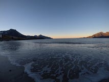 Beautiful calm blue waves hitting white frozen sandy beach in late autumn in the arctic circle with deep mountain and open sea vie Royalty Free Stock Photo Beautiful calm blue waves hitting white frozen sandy beach in late autumn in the arctic circle with deep mountain and open sea vie Royalty Free Stock Photo