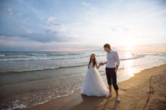 A beautiful couple of newlyweds, the bride and groom walking on the beach. Gorgeous sunset and sky. Wedding dresses, a stock image A beautiful couple of newlyweds, the bride and groom walking on the beach. Gorgeous sunset and sky. Wedding dresses, a stock image