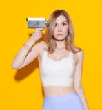 Beautiful fashionable girl posing and holding near a temple in surprise vintage movie camera in a top and a skirt on a yellow back stock photography Beautiful fashionable girl posing and holding near a temple in surprise vintage movie camera in a top and a skirt on a yellow back stock photography