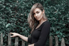 Beautiful girl in a black shirt standing near the wooden fence. At the background of green foliage Stock Image Beautiful girl in a black shirt standing near the wooden fence. At the background of green foliage Stock Image