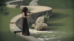 Beautiful girl in dress plays violin outdoors. Elegant violinist in forest stock video footage Beautiful girl in dress plays violin outdoors. Elegant violinist in forest stock video footage