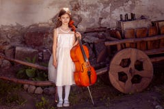 Beautiful girl in a pink dress with a cello in the village