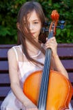 Beautiful girl in a pink dress sits on a bench with a cello