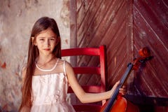 Beautiful girl in a pink dress sits on a red chair with a cello