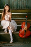 Beautiful girl in a pink dress sits on the steps with a cello in a country house