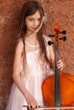 Beautiful girl in a pink dress stands with a cello in the city against the wall