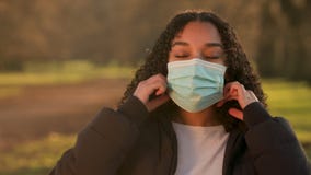 African American girl biracial teenager young woman outside taking off a face mask during COVID-19 Coronavirus pandemic