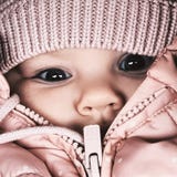 beautiful little girl looks with large eyes behind hats and jackets