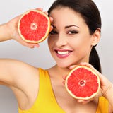 Beautiful makeup brunette woman holding fresh red grapefruit near the face and looking happy on empty space blue background. royalty free stock photography Beautiful makeup brunette woman holding fresh red grapefruit near the face and looking happy on empty space blue background. royalty free stock photography