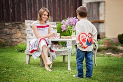 Beautiful mom, having coffee in a backyard, young cute child giving her present and flowers royalty free stock photography Beautiful mom, having coffee in a backyard, young cute child giving her present and flowers royalty free stock photography