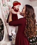 Beautiful mother with luxurious dark hair posing with her cute little girl beside Christmas tree Stock Images Beautiful mother with luxurious dark hair posing with her cute little girl beside Christmas tree Stock Images