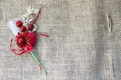 A beautiful red artificial flower with a green stem on the texture of a brown old linen cloth, linen natural material with a rough. Perpendicular interlacing of Royalty Free Stock Photo A beautiful red artificial flower with a green stem on the texture of a brown old linen cloth, linen natural material with a rough. Perpendicular interlacing of Royalty Free Stock Photo