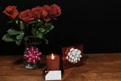 Beautiful red roses in vase with pink bow wrapped present and red candle with name tag on wooden table on dark background stock photo Beautiful red roses in vase with pink bow wrapped present and red candle with name tag on wooden table on dark background stock photo