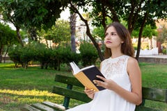 Beautiful school or college girl is sitting on the bench with a book in the hands and thinking about something in the park stock photography Beautiful school or college girl is sitting on the bench with a book in the hands and thinking about something in the park stock photography