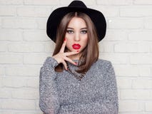 Beautiful young girl in a black hat with red full lips, bright makeup and painted my nails red