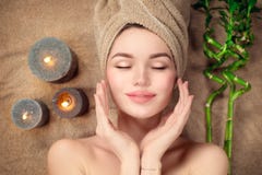 Beautiful spa woman with a towel on her head lying and touching face skin. Skincare