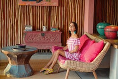 Beautiful tanned woman sitting on a pink sofa and posing. Interior in ethnic style stock photo Beautiful tanned woman sitting on a pink sofa and posing. Interior in ethnic style stock photo
