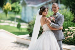 Beautiful wedding couple hugging in park with green trees on background. Groom in a business gray suit, white shirt in a royalty free stock photos Beautiful wedding couple hugging in park with green trees on background. Groom in a business gray suit, white shirt in a royalty free stock photos
