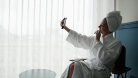 Beautiful woman in bathrobe, with towel on her head, take selfie on mobile phone stock video footage Beautiful woman in bathrobe, with towel on her head, take selfie on mobile phone stock video footage