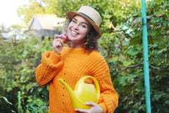 Beautiful woman with curly brown hair holding yellow watering can and apple