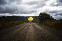 Beautiful woman hold yellow umbrella and walks on a country road under rain Royalty Free Stock Images Beautiful woman hold yellow umbrella and walks on a country road under rain Royalty Free Stock Images