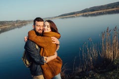 Travel and love. Happy young couple walking along the shore of blue lake in hipster clothes. Beautiful young couple in hipster clothes hugging in the background royalty free stock photos Travel and love. Happy young couple walking along the shore of blue lake in hipster clothes. Beautiful young couple in hipster clothes hugging in the background royalty free stock photos