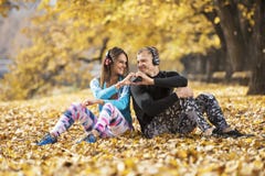 Beautiful young couple resting and listening music after successful training in the park. Hand shape heart. Royalty Free Stock Photography Beautiful young couple resting and listening music after successful training in the park. Hand shape heart. Royalty Free Stock Photography