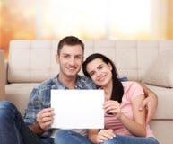 Beautiful young couple is smiling and showing blank paper while sitting on the floor in new apartment. stock images Beautiful young couple is smiling and showing blank paper while sitting on the floor in new apartment. stock images