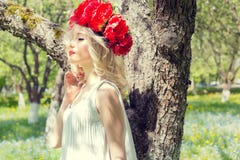 Beautiful young gentle elegant young blond woman with red peony in a wreath of white blouse walking in the lush apple orchard Royalty Free Stock Images Beautiful young gentle elegant young blond woman with red peony in a wreath of white blouse walking in the lush apple orchard Royalty Free Stock Images
