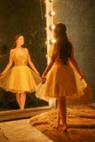 Beautiful young girl in a gold evening dress stands on a fur rug near a large mirror in a frame with lights and looks into her ref stock images Beautiful young girl in a gold evening dress stands on a fur rug near a large mirror in a frame with lights and looks into her ref stock images