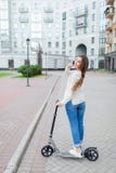 Beautiful young girl with long brown hair stopped while riding the scooter to talk to a friend on the phone on the background of t Stock Images Beautiful young girl with long brown hair stopped while riding the scooter to talk to a friend on the phone on the background of t Stock Images