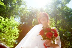 Beautiful young happy bride standing near green trees in a park and holding a beautiful bouquet.