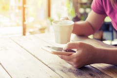 Beautiful Young Hipster Woman`s Hands Holding Mobile Smart Phone With Hot Coffee Cup At Cafe Shop Stock Photo