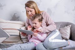 Beautiful young mother and her little daughter are watching movies together and playing on the tablet while sitting on the sofa. royalty free stock photos Beautiful young mother and her little daughter are watching movies together and playing on the tablet while sitting on the sofa. royalty free stock photos