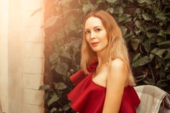 A beautiful young woman in an asymmetrical red-burgundy cocktail dress on one shoulder sits in a restaurant and happily smiles stock image A beautiful young woman in an asymmetrical red-burgundy cocktail dress on one shoulder sits in a restaurant and happily smiles stock image