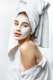 Beautiful young woman dressed in white clothes with a white towel on her hair and cosmetic mask on her face holds her royalty free stock photography Beautiful young woman dressed in white clothes with a white towel on her hair and cosmetic mask on her face holds her royalty free stock photography