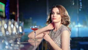 Beautiful young woman drinking cocktail sitting on bar looking at camera at disco party stock video Beautiful young woman drinking cocktail sitting on bar looking at camera at disco party stock video