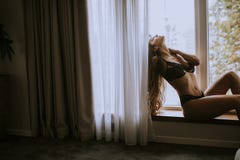 Beautiful young woman in lingerie sitting and looking outside the window in beautiful apartment