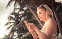 Beautiful young woman traveler in bikini on beach texting smartphone during beach holidays royalty free stock photo Beautiful young woman traveler in bikini on beach texting smartphone during beach holidays royalty free stock photo