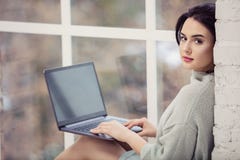Beautiful young woman using laptop while sitting by window Stock Photography Beautiful young woman using laptop while sitting by window Stock Photography