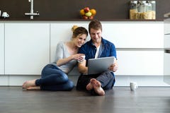 Beaux jeunes couples au moyen de eux comprimé numérique dans la cuisine Photographie stock libre de droits Beaux jeunes couples au moyen de eux comprimé numérique dans la cuisine Photographie stock libre de droits