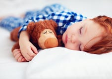 Bebé adorable del niño del pelirrojo en pijamas de la franela que duerme con el juguete del calentador de la felpa Foto de archivo libre de regalías Bebé adorable del niño del pelirrojo en pijamas de la franela que duerme con el juguete del calentador de la felpa Foto de archivo libre de regalías