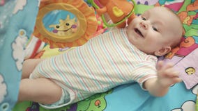 Bebé alegre que miente en la estera colorida Niño feliz que juega en la estera que se convierte almacen de video Bebé alegre que miente en la estera colorida Niño feliz que juega en la estera que se convierte almacen de video