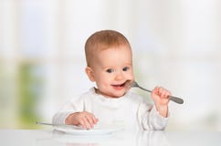 Bebé divertido con un cuchillo y una bifurcación que come la comida imagen de archivo libre de regalías Bebé divertido con un cuchillo y una bifurcación que come la comida imagen de archivo libre de regalías
