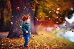bebé feliz del niño del pelirrojo que se divierte, jugando con las hojas caidas en parque del otoño bebé feliz del niño del pelirrojo que se divierte, jugando con las hojas caidas en parque del otoño