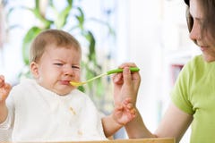 Bebé hambriento que come la comida al lado de su madre. Fotos de archivo Bebé hambriento que come la comida al lado de su madre. Fotos de archivo